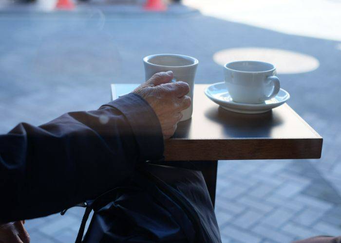 An old man reaches for his coffee mug while looking out onto the streets of Asakusa.